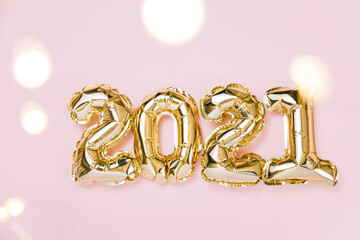 Happy New year 2021 celebration. Gold foil balloons numeral 2021 and fairy lights on pastel pink background. Flat lay, christmas creative concept