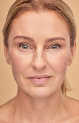 Close up of beautiful mature woman looking at camera isolated over beige background in studio,...