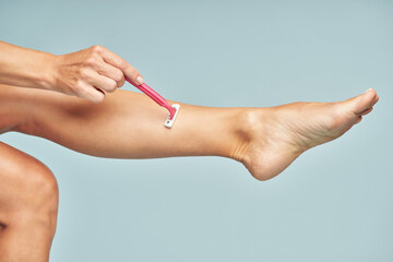 Hair Removal. Close up of lady shaving her leg with safety razor isolated on blue background.