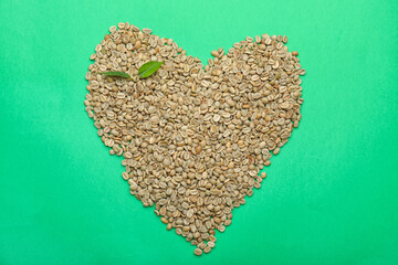 Heart shape made of green coffee beans on color background