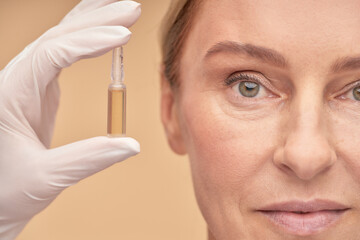 Beautician in a glove holding an ampoule with hyaluronic acid