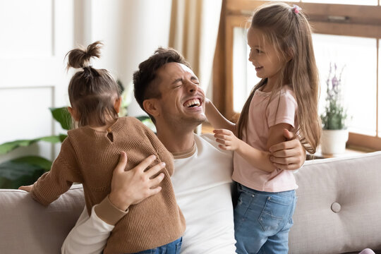 Cheerful father spend funny pleasant time with 6s 7s cute little daughters, family laughing enjoy weekend together on couch at home. Happy fatherhood, next generation, offspring, life value concept