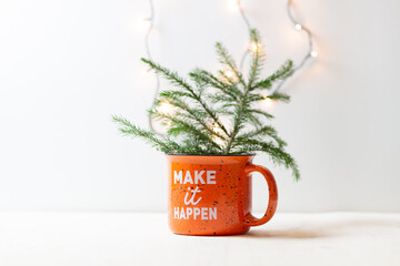 Cap with words  "make it happen" and fir tree branch on white background with lights garland