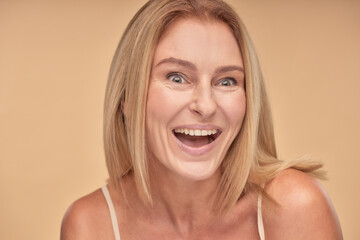 Close up portrait of excited mature woman posing in studio over beige background