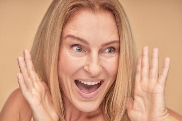 Close up portrait of excited mature woman with surprised look over beige background