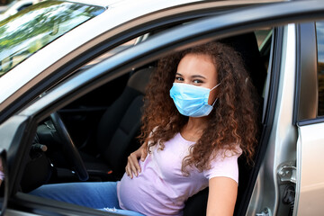 Pregnant African-American woman wearing medical mask in car