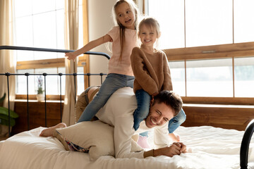 In bedroom two little cheery daughters play with dad, saddled him seated on his back. Laughing...