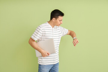 Young man with wristwatch and laptop on color background