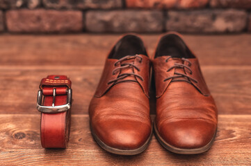 Classic men's brown leather shoes with a belt on a wooden background.