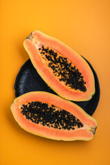 Halves of papaya fruit on a black plate over an orange background, top view