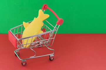 Shopping basket on a red and green background with a plastic fish inside. The concept of unnatural...