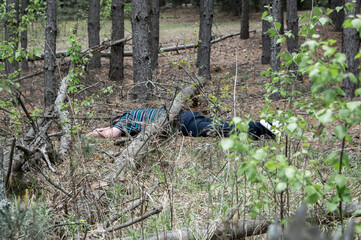 A body in the woods. A dead man in a blue t-shirt and trousers is pinned down by a fallen tree. Concept of accidents in the forest.