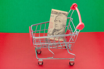 Shopping cart on a red and green background with money inside. The concept of reducing purchasing...