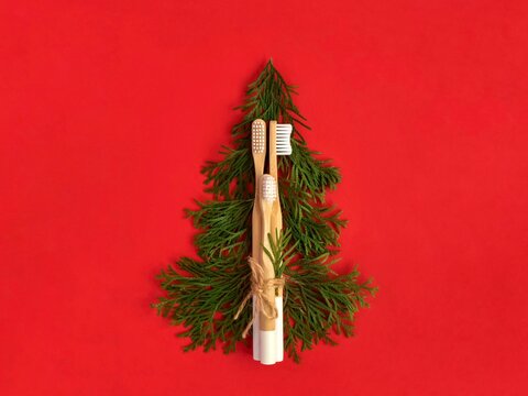 Bamboo toothbrushes tied with natural rope. White cedar branches in the shape of a Christmas tree on the red background. Plastic free, zero waste.