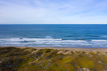Waves from the Pacific Ocean wash onto an empty beach and sand dunes in Morro Bay, California. This coastal part of Central California is known for its beautiful natural scenery.