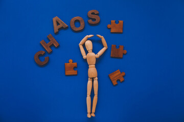 Wooden mannequin with word CHAOS and puzzle pieces on color background