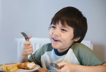 Healthy kid eating fried battered fish fillet for brunch, Happy young boy eaitng fish and chips for...