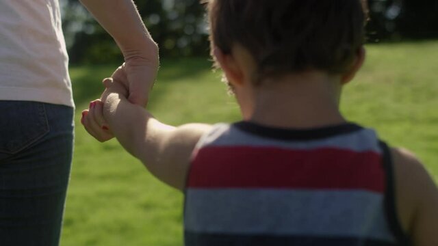Close-up of a young boy hold his mom's hands as they walk through the park