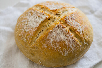 bacon of fresh homemade white bread with white flour and a cross in the center on a white tea towel