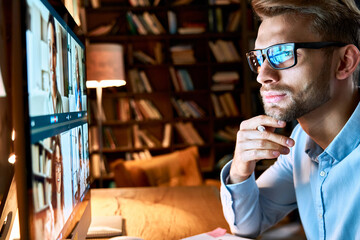 Serious young businessman wearing glasses looking at pc computer screen working online by video...