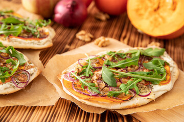 gebackener Flammkuchen mit Kürbis vom Hokkaido, Apfel, Zwiebelringen, Walnüssen, Frischkäse, Schmand, Rosmarin und Rucola auf einem Tisch aus Holz in der Küche