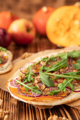 gebackener Flammkuchen mit Kürbis vom Hokkaido, Apfel, Zwiebelringen, Walnüssen, Frischkäse, Schmand, Rosmarin und Rucola auf einem Tisch aus Holz in der Küche