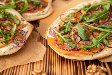 gebackener Flammkuchen mit Kürbis vom Hokkaido, Apfel, Zwiebelringen, Walnüssen, Frischkäse, Schmand, Rosmarin und Rucola auf einem Tisch aus Holz in der Küche
