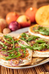 gebackener Flammkuchen mit Kürbis vom Hokkaido, Apfel, Zwiebelringen, Walnüssen, Frischkäse, Schmand, Rosmarin und Rucola auf einem Tisch aus Holz in der Küche