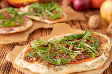 gebackener Flammkuchen mit Kürbis vom Hokkaido, Apfel, Zwiebelringen, Walnüssen, Frischkäse, Schmand, Rosmarin und Rucola auf einem Tisch aus Holz in der Küche