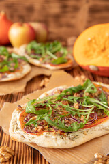 gebackener Flammkuchen mit Kürbis vom Hokkaido, Apfel, Zwiebelringen, Walnüssen, Frischkäse, Schmand, Rosmarin und Rucola auf einem Tisch aus Holz in der Küche