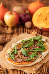 gebackener Flammkuchen mit Kürbis vom Hokkaido, Apfel, Zwiebelringen, Walnüssen, Frischkäse, Schmand, Rosmarin und Rucola auf einem Tisch aus Holz in der Küche