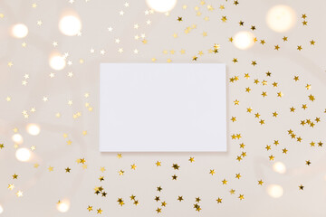 Festive gold background. Empty paper blank, shining stars confetti and fairy lights on beige and...
