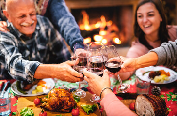 People toasting red wine glass having fun at Christmas supper reunion - Holiday celebration concept with happy family sharing winter time together at home fireplace - Warm filter with focus on hands