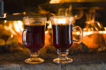 two glasses of mulled wine, standing on gray bricks against the flame of fire