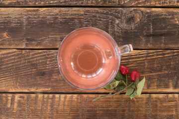 Rosehip tea in a glass cup and a sprig of rosehip with berries nearby on a wooden table. Rustic style, top view, flat lay