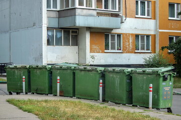 Fototapeta na wymiar Six green trash cans standing in an uneven line near a residential high rise