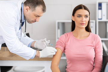 Male doctor doing vaccination against coronavirus to young woman