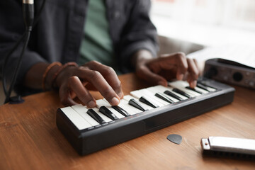 Close up of unrecognizable African-American man playing music on keyboard while composing at home,...