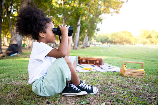 Mixed-race girl looking natural and using binoculars in public park with a happy face standing and smiling. Concept of nature and wildlife studies.