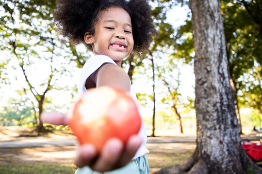 Mixed-race girl holding red apple and have big smile face in the park. She relax and playing in the public. Learning ideas outside the classroom. Soft focus