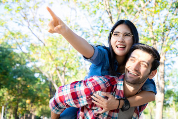 Man giving piggyback ride to girlfriend with bright smile and looking at natural in the public park. Soft focus and blur