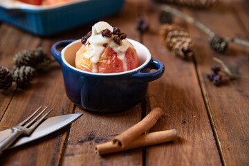 gebackener Bratapfel mit Füllung aus Marzipan, Mandeln, Rosinen und Zimt mit Vanillesoße zur Winterzeit und Weihnachten auf einem braunen Tisch aus Holz in der Küche