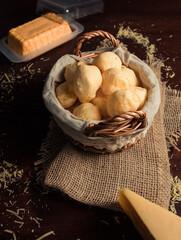Cheese bread 'pao de queijo' basket with slice of cheese, and grated cheese on rustic wooden table.