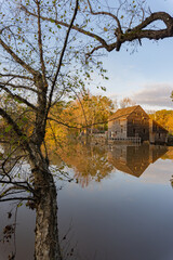 Obraz premium Reflection of the historic Yates Mill wooden building in the waters of a pond in autumn at dusk framed by colorful trees; vertical image
