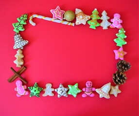 Christmas composition: frame of Christmas cookies, candy cane, pine cones, cinnamon sticks and a golden ball on a red background