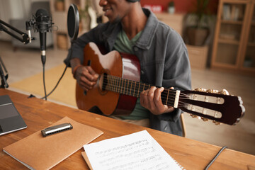 Cropped portrait of talented African-American man singing to microphone and playing guitar while recording music in studio, copy space