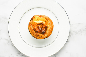 A picture of freshly baked egg tart on white plate at marble table. Famous Macao, Malaysia and Portugal snack food.