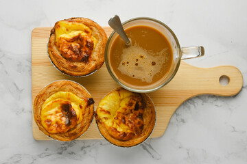 A picture of freshly baked 3 egg tarts with milk coffee on wooden board.