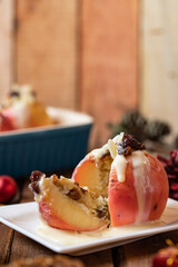 gebackener Bratapfel mit Füllung aus Marzipan, Mandeln, Rosinen und Zimt mit Vanillesoße zur Winterzeit und Weihnachten auf einem braunen Tisch aus Holz in der Küche