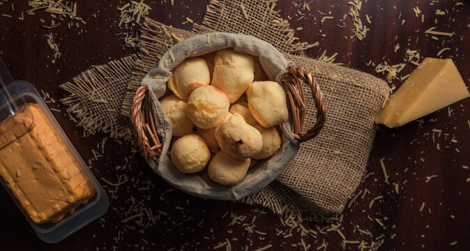 Cheese bread 'pao de queijo' basket with slice of cheese, and grated cheese on rustic wooden table. Top View